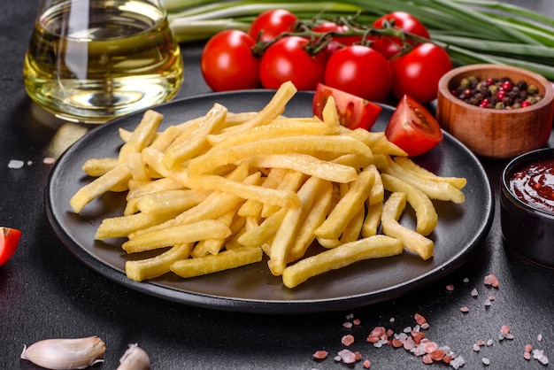 Fresh hot french fries with salt vegetables and spices on a dark concrete background