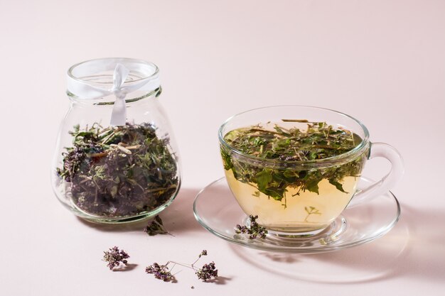 Fresh hot tea with oregano in a cup and dry herb in a jar. Herbal medicine and alternative therapy