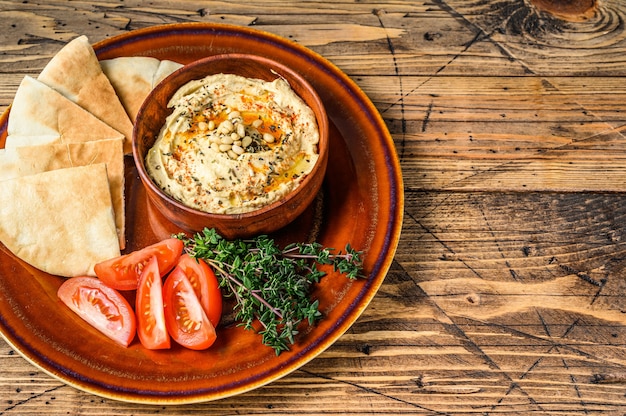 Hummus fresco con pane pita, pomodoro e prezzemolo su un piatto rustico. fondo in legno. vista dall'alto. copia spazio.