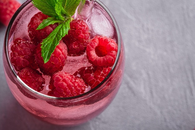 Fresh ice cold berry juice drink with mint, summer raspberry lemonade in glass with straws on stone concrete, angle view macro