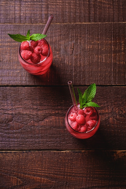 Fresh ice cold berry juice drink with mint, summer raspberry lemonade in two glass with straws on brown wooden background, angle view selective focus