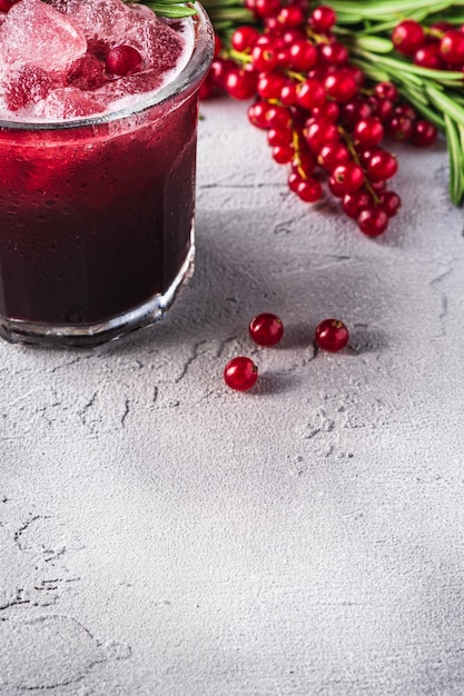 Fresh ice cold fruit cocktail in glass, refreshing summer red currant berry drink with rosemary leaf on stone concrete table, angle view copy space