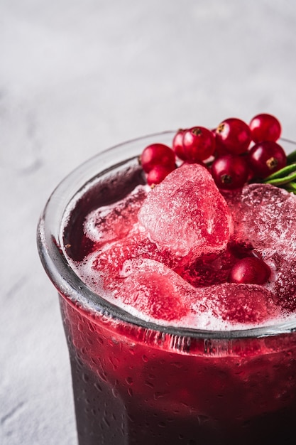 Fresh ice cold fruit cocktail in glass, refreshing summer red currant berry drink with rosemary leaf on stone concrete table, angle view macro