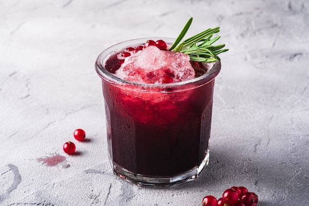 Fresh ice cold fruit cocktail in glass, refreshing summer red currant berry drink with rosemary leaf on stone concrete table, angle view