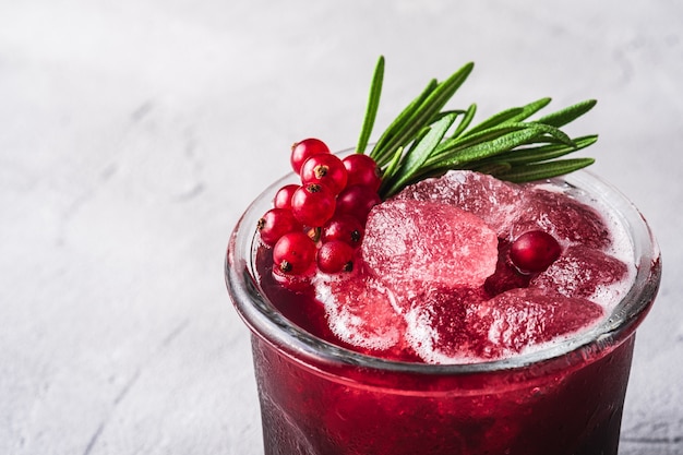 Cocktail di frutta ghiacciata fresca in vetro, rinfrescante bevanda estiva a bacca di ribes rosso con foglie di rosmarino