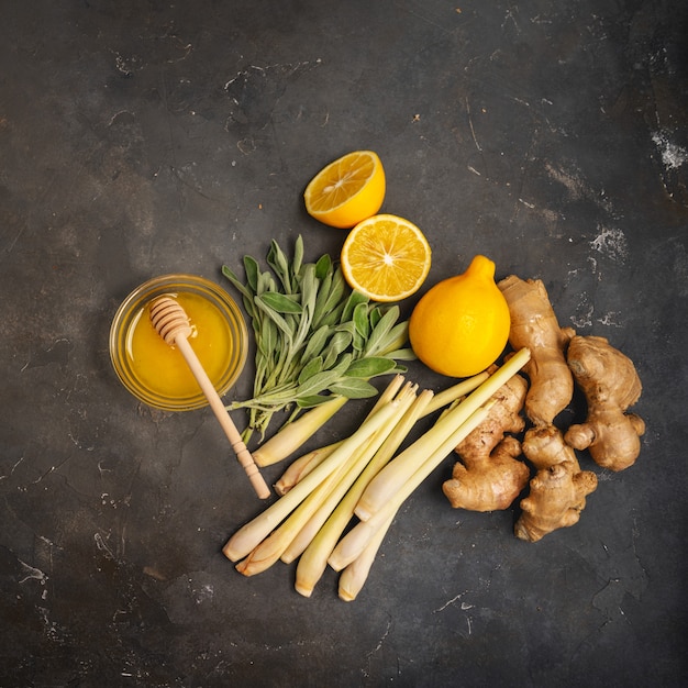 Fresh ingredients ginger, lemongrass, sage, honey and lemon for healthy antioxidant and anti-inflammatory ginger tea on dark background with copy space. Top view.