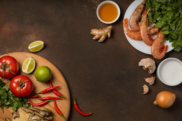 Fresh ingredients of tom yum soup on a tray and plate on a dark background, top view