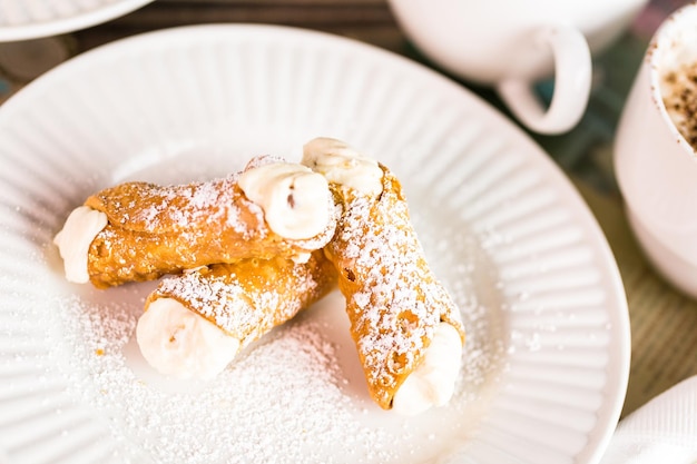 Cannoli italiani freschi con caffè sul tavolo.