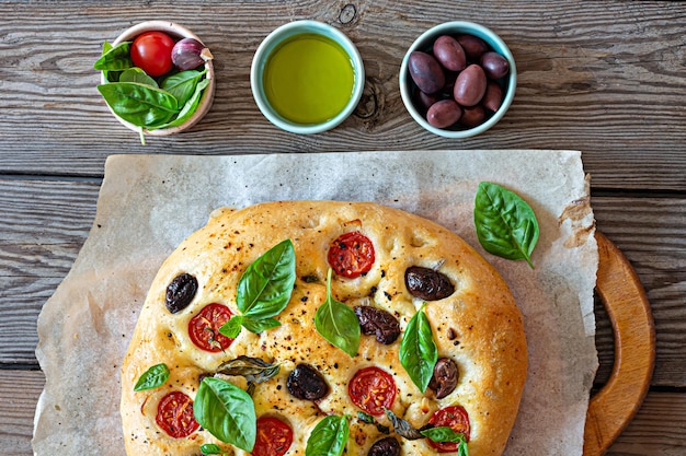 Fresh Italian flat bread Focaccia with tomatoes, olives, garlic and herbs on a wooden background.