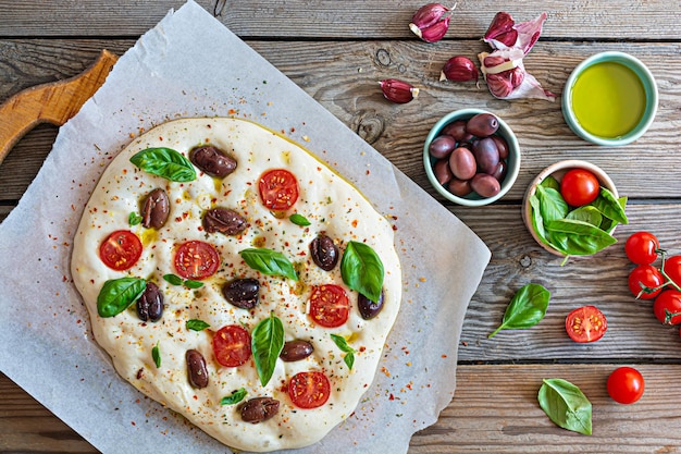 Fresh Italian flat bread (raw) Focaccia with tomatoes, olives, garlic and herbs