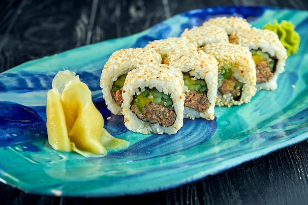 Fresh, Japanese sushi rolls with avocado, cucumber and ????, served in a plate with wasabi and ginger on a dark surface. Japanese kitchen. California roll in sesame