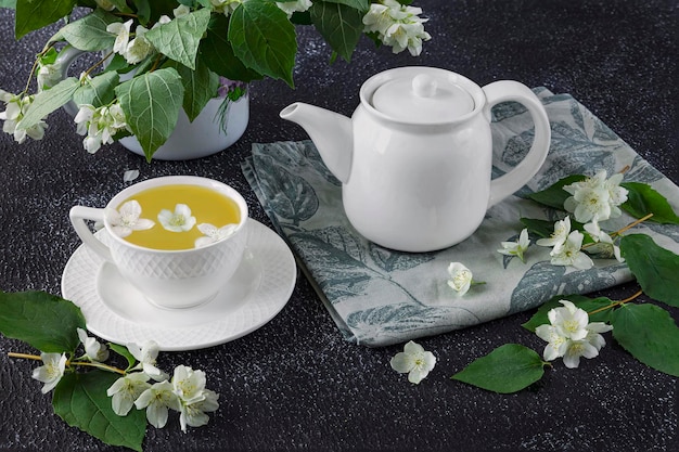 Fresh jasmine flowers in a vase green tea with jasmine in a white cup and teapot