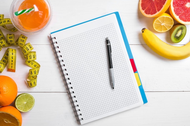 Fresh juice in glass from citrus fruits  lemon grapefruit orange notebook with pencil on white woode...