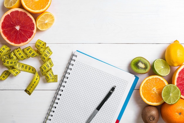 Fresh juice in glass from citrus fruits  lemon grapefruit orange notebook with pencil on white woode...