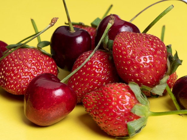 Fresh juicy cherries and strawberries on a bright yellow background. Healthy food, vegetarianism, close-up