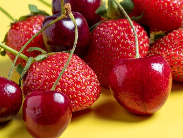 Fresh juicy cherries and strawberries on a bright yellow background. Healthy food, vegetarianism, close-up.