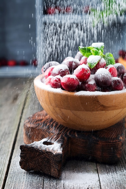 Fresh juicy cranberries with sugar powder in a bamboo bowl on the old wooden surface. Selective focus.