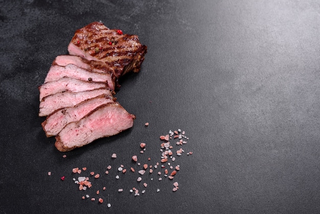 Fresh juicy delicious beef steak on a dark background. Meat dish with spices and herbs