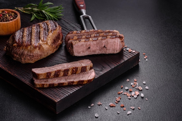 Свежий сочный вкусный стейк из говядины на темном фоне. Мясное блюдо со специями и травами