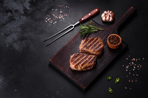Фото Свежий сочный вкусный стейк из говядины на темном фоне. мясное блюдо со специями и травами