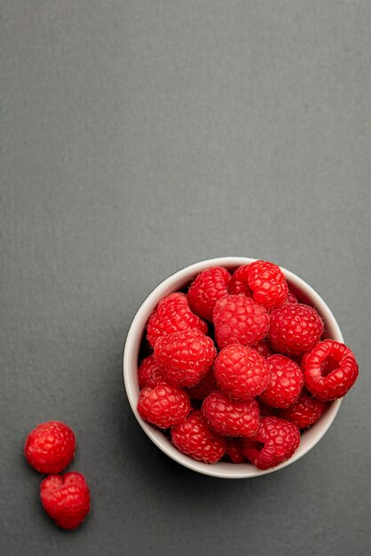 Fresh juicy raspberries in a small black plate. bright red crimson close-up. summer berry picking time. healthy organic fruits for kids. vertical photo