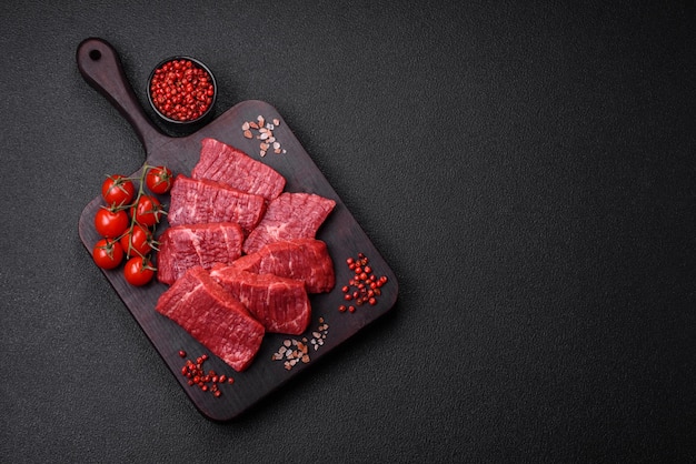 Fresh juicy raw beef slices with salt and spices on a dark concrete background