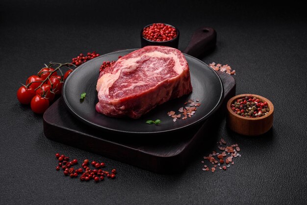 Fresh juicy raw beef striploin steak with salt and spices on a dark concrete background