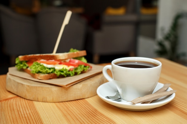 Fresh juicy sandwich with cup of hot coffee on wooden table with dark background