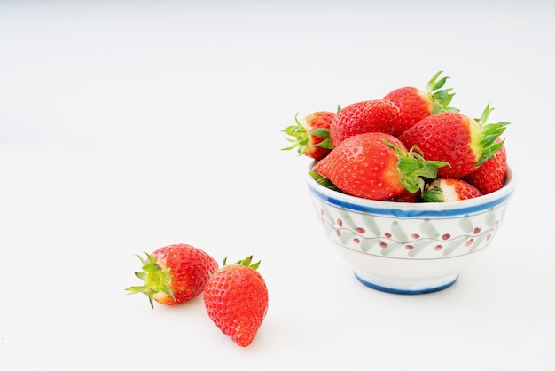 Fresh juicy strawberries in the bowl isolated on a white desk. Side view. Copy space