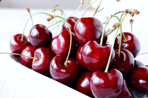 Photo fresh juicy sweet dark red sweet cherry in a white ceramic bowl on a light wooden background