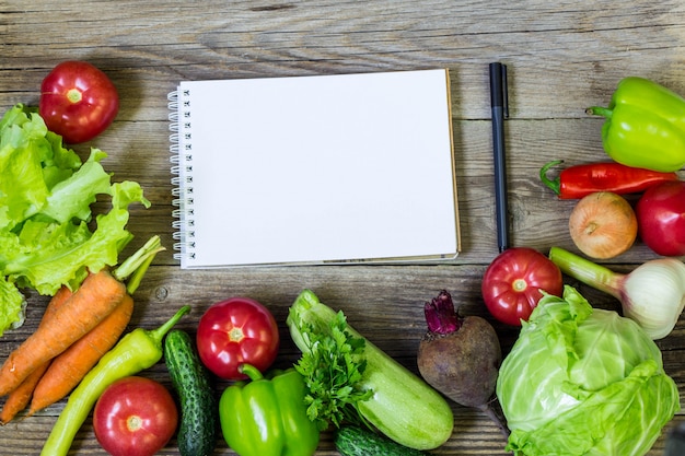 Fresh juicy vegetables border, blank white notepad, top view