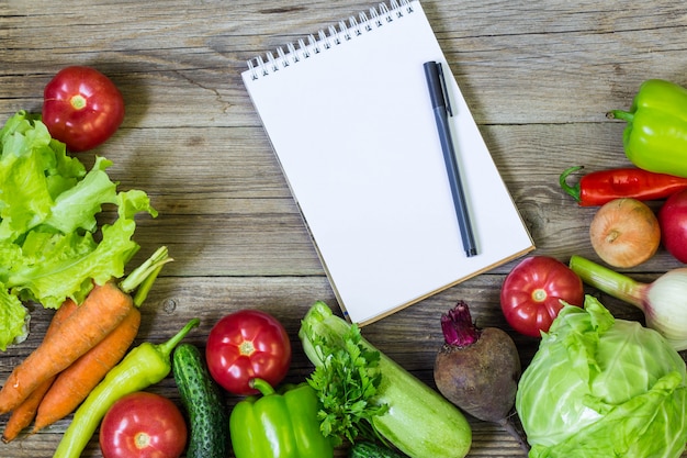 Fresh juicy vegetables border, blank white notepad 