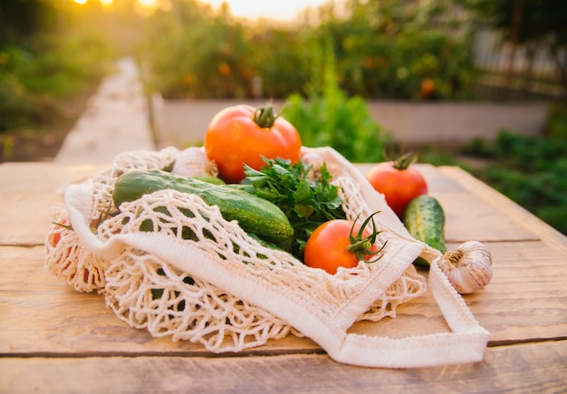 Fresh juicy vegetables products in a reusable shopping bag a string bag made of recycled materials on a wooden table in the garden Vegetarianism No plastic Ecofriendly lifestyle