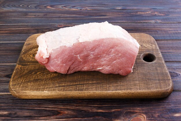 木製の背景の木製のカッティングボードのトップビューの新鮮な大きな豚肉