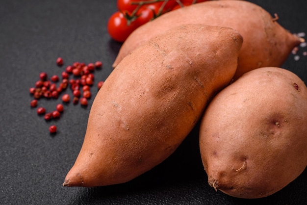 Fresh large pink sweet potato tubers with tomatoes and spices on a dark background cooking a healthy vegetarian meal