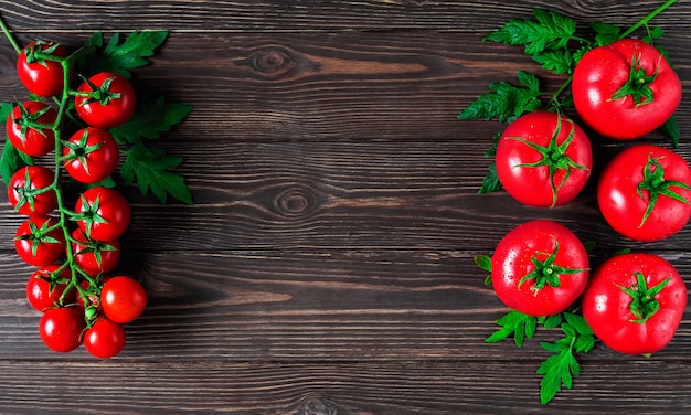 Fresh large tomatoes and a branch of cherry tomatoes with leaves on a dark wooden surface