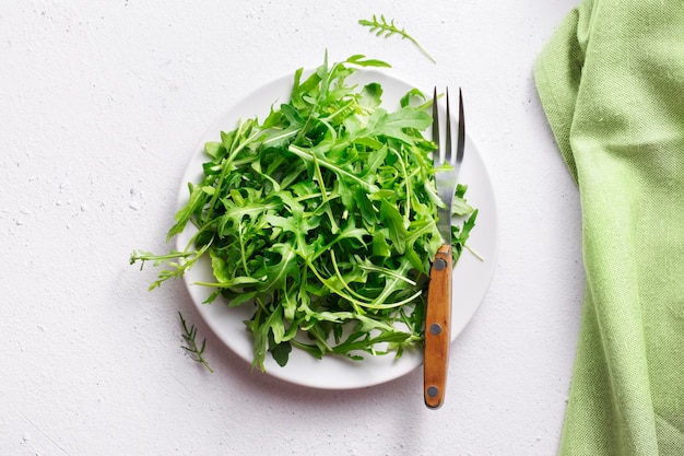 Fresh leaves of arugula in a plate on a white background, top view.