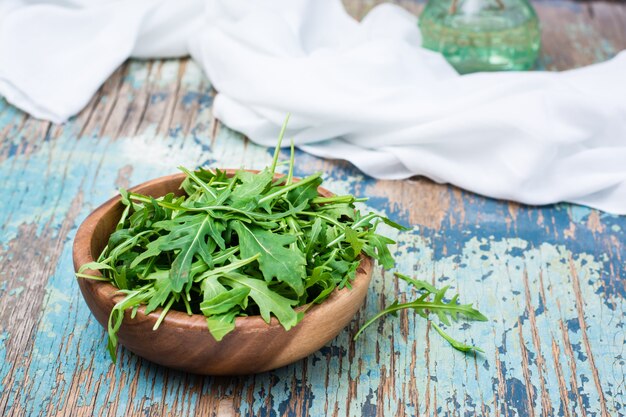 Fresh leaves of arugula in a wooden bowl and white napkin on a wooden table