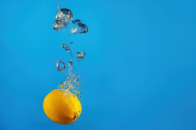 Fresh lemon falls into the water with a splash on a blue background