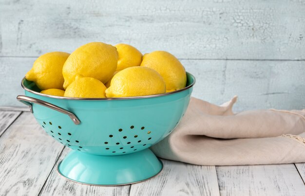 Fresh lemons in blue colander. Wooden background