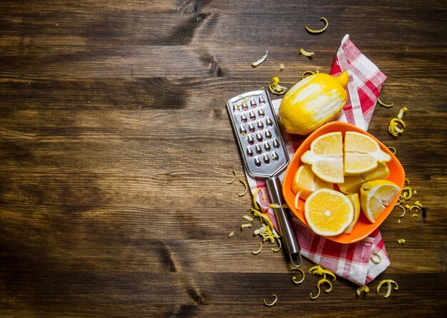 Fresh lemons in the bowl with the zest and grater on fabric on a wooden table. Top view