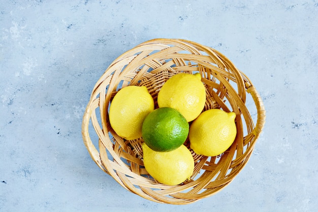 Fresh lemons and limes in a basket on a blue background. Citrus fruit.