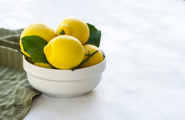 Fresh lemons with green leaves in bowl on white background Copy space