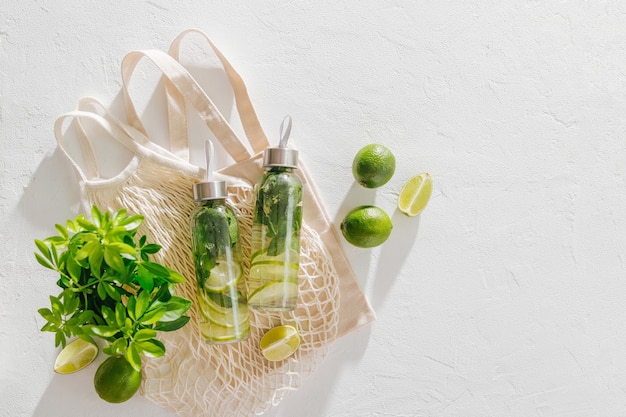 Fresh lime and mint infused water, cocktail, detox drink, lemonade in reusable bottles with eco bags. Eco friendly. Sustainable lifestyle.