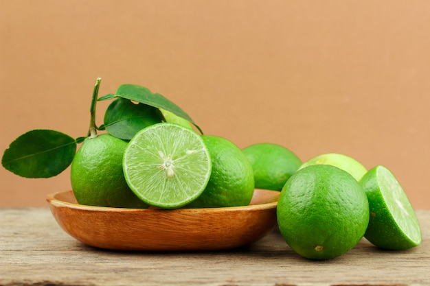 Fresh limes in wooden bowl on wooden background