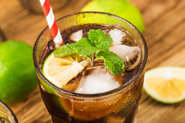 Fresh made Cuba Libre with brown rum, cola, mint and lemon on wooden table