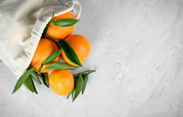 Fresh mandarin citrus fruits in flax burlap bag on grey cement background. Copy space.