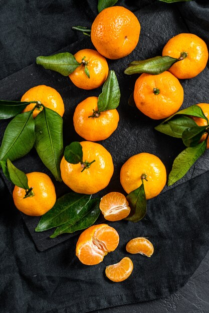 Fresh mandarin oranges fruit or tangerines with leaves in a wooden bowl. Gray background. Top view