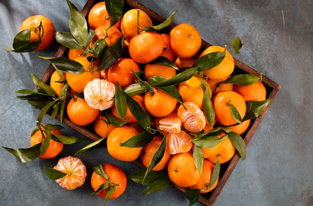 Fresh mandarin oranges fruit or tangerines with leaves in wooden box, top view