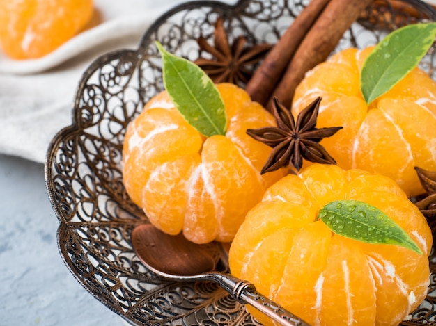 Fresh mandarins in a plate with fir tree branches, star anise cinnamon on gray